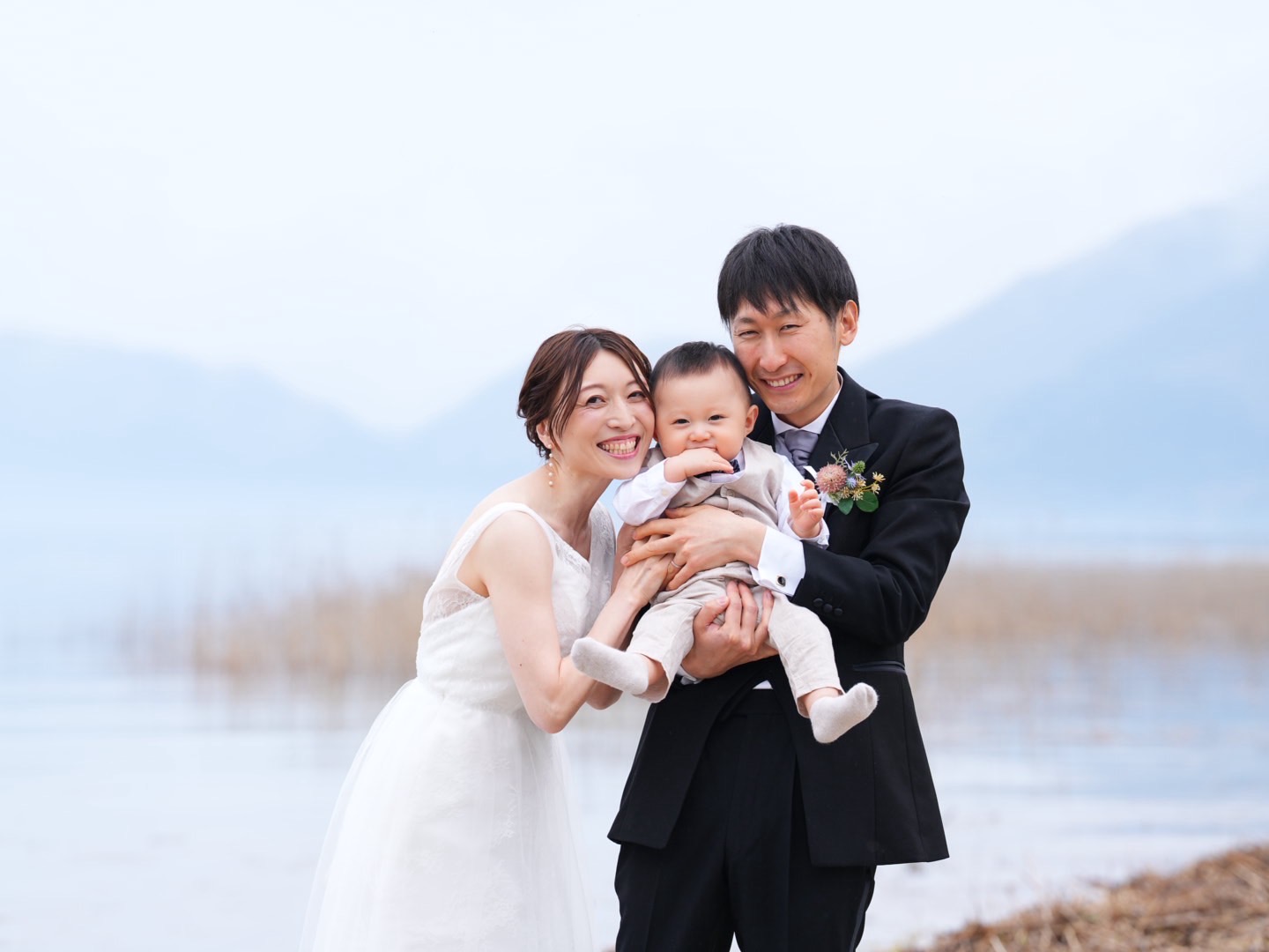 田沢湖畔で新郎新婦とお子さまが笑顔で写る、実際のフォトウェディング写真。