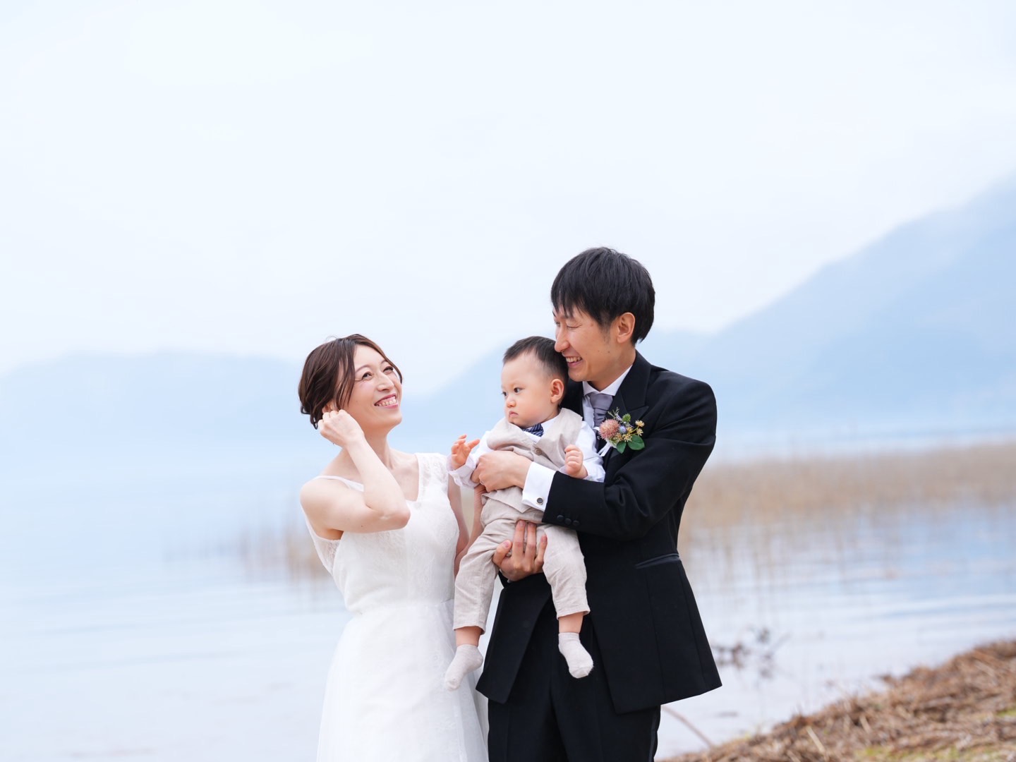 田沢湖畔で新郎新婦とお子さまが向き合う、実際のフォトウェディング写真。