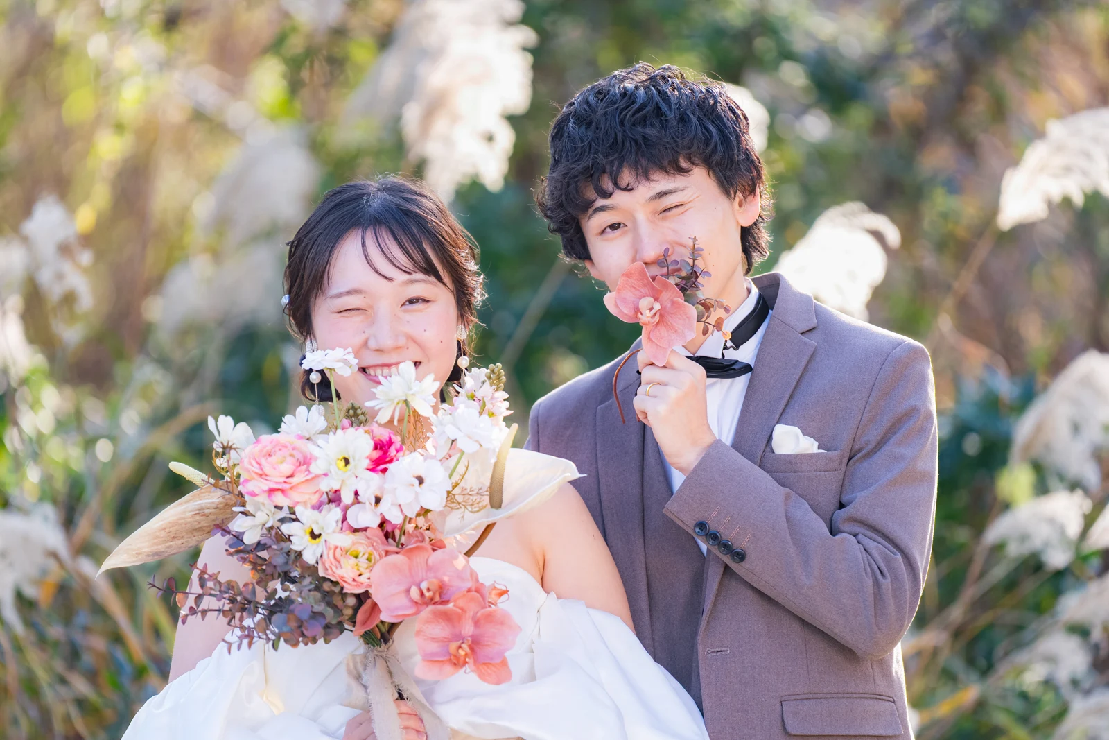 花束を持ち、緑の中で笑顔を見せるドレスとタキシード姿のおふたり
