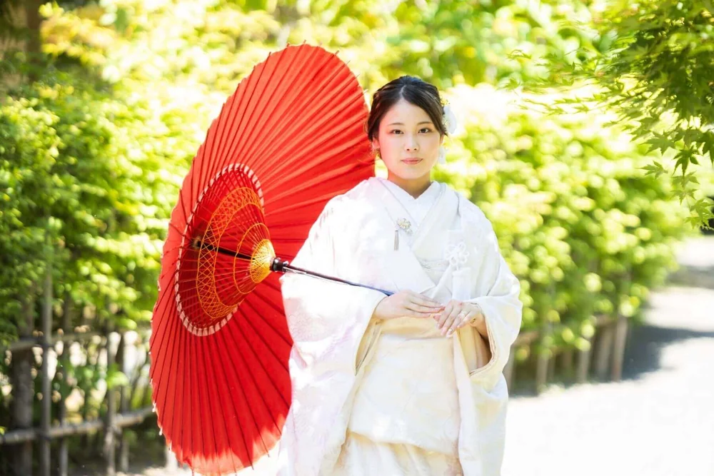 藤田記念庭園の緑を背景に赤い和傘を差す白無垢の花嫁