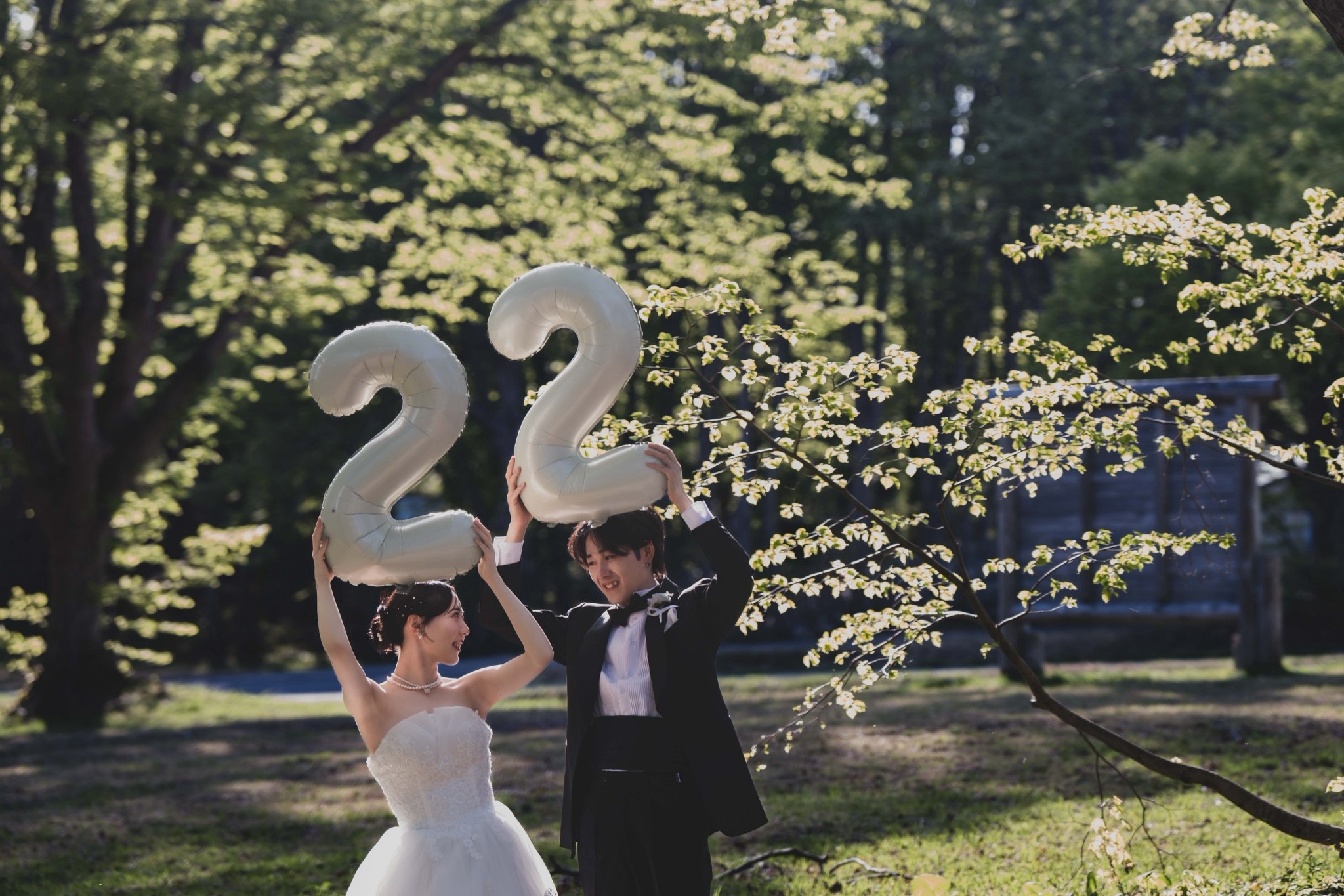 緑の中で数字の風船を持ち、笑顔を交わすドレス姿の新婦と新郎