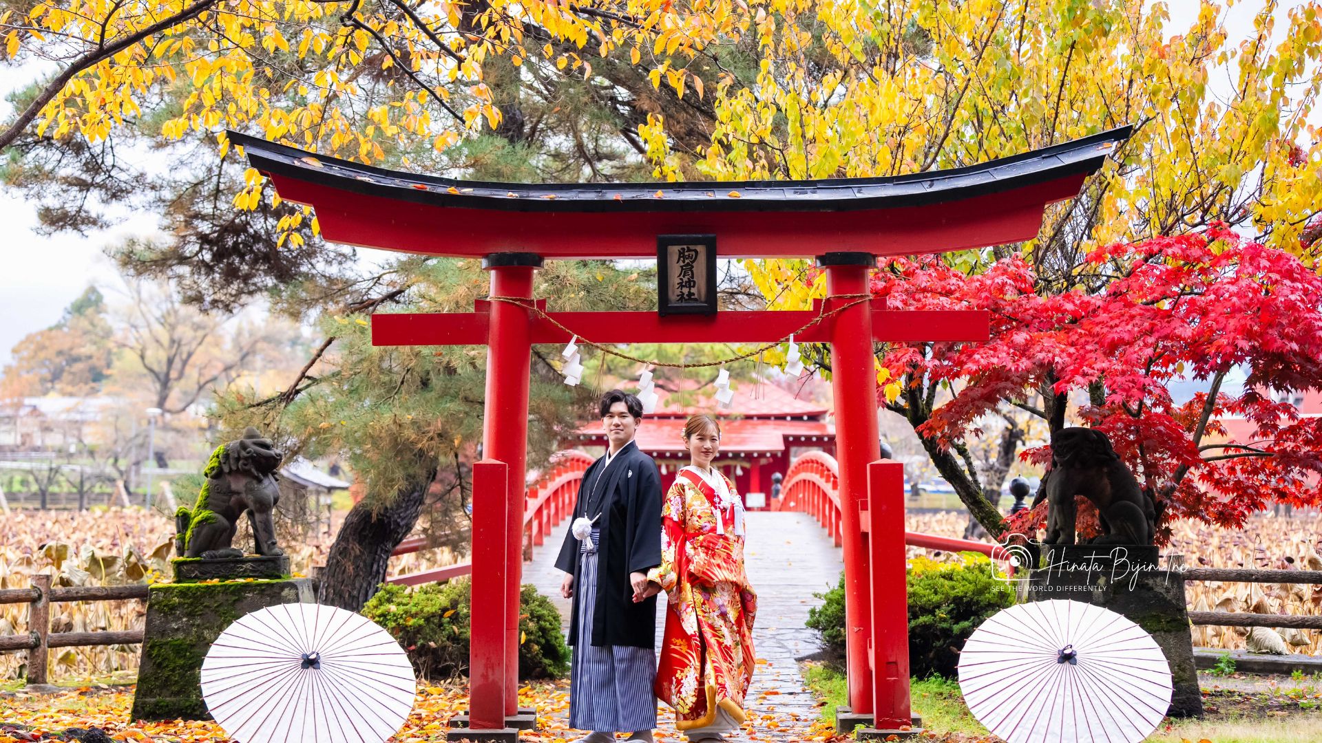 紅葉と赤い鳥居を背景に並ぶ和装の新郎新婦